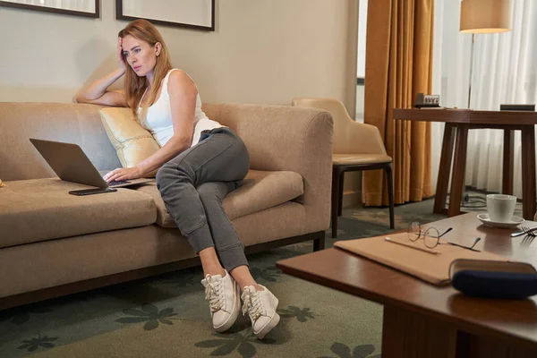 Mujer seria en suite de hotel utilizando el ordenador portátil en el sofá — Foto de Stock