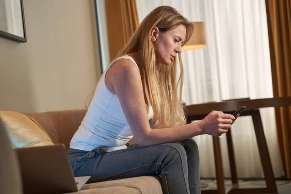 Заинтересованная женщина на диване щелкает своим мобильным телефоном — стоковое фото