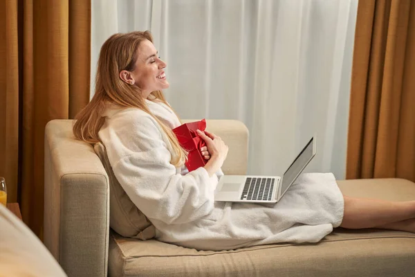 Njuten kvinna njuter av sin present på soffan i hotellets svit — Stockfoto