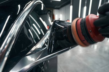 Eldivenli el cilasıyla arabanın dış cephesini cilalıyor.