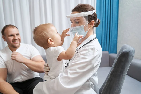 Ärztin hält Baby in der Hand und greift nach ihrem Gesichtsschutz — Stockfoto