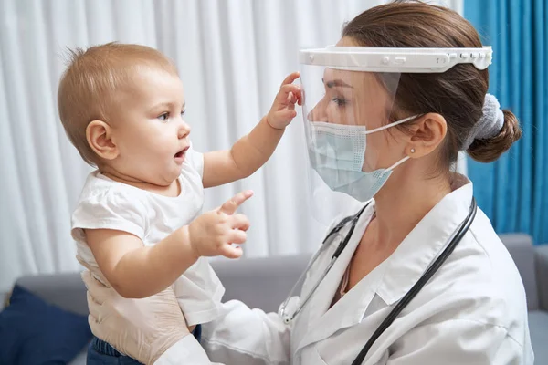 Lekarz wychowujący dziecko, który dotyka jej tarczy twarzy — Zdjęcie stockowe