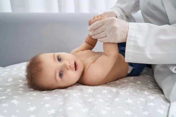 Therapist holding baby hands while it lying on bed — Stock Photo, Image