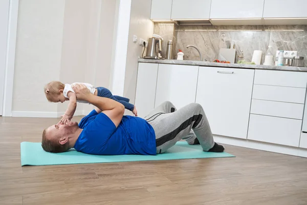 Homem encantado rindo quando o bebê tocando seu rosto durante o exercício — Fotografia de Stock