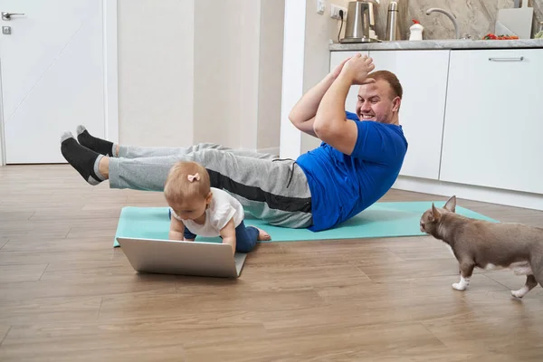 Man gör buken crunches medan stirrar på barnet nära laptop — Stockfoto