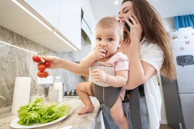 Evde çocukla vakit geçirirken birden fazla iş yapan beyaz bir anne telefonda konuşuyor.