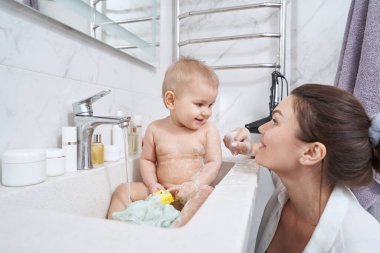 Banyo lavabosundaki tatlı küçük çocuk vanadan çıkan suyla yıkıyor.