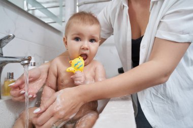 Banyodaki lavabodaki fotoğraf makinesine bakan banyo oyuncağıyla sevimli bir bebek.