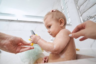 Bebek banyo yaparken oyuncak balık alıyor.