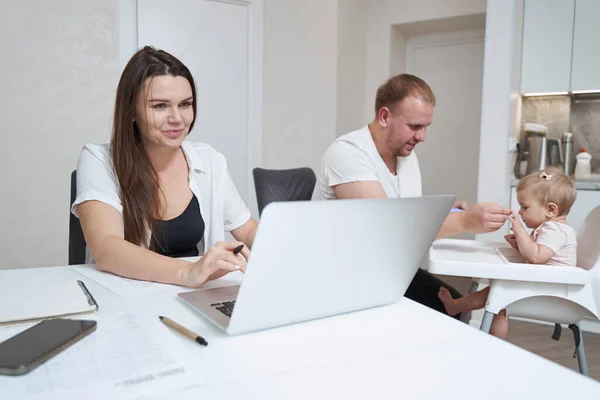 Beautiful Caucasian mom looking to the screen of computer and her family in the kitchen — Stock Photo, Image