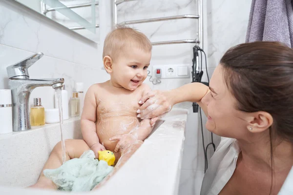 Cute baby in bathroom sink washing in water from valve — Stock Photo, Image