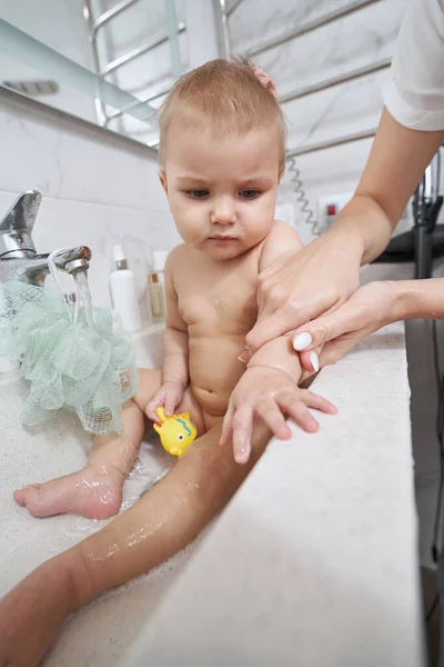 Baby looking at person, grabbing its hand during bath — Stock Photo, Image