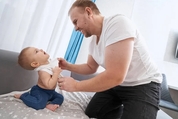 Père excité habillant bébé en T-shirt sur canapé — Photo