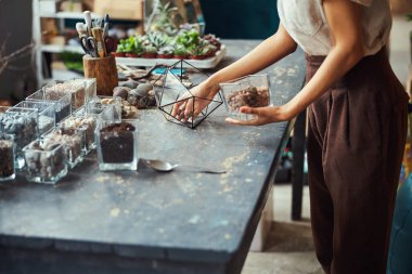 Elinde cam vazo olan bir çiçekçi, teraryum kabının üzerine eğilmiş.
