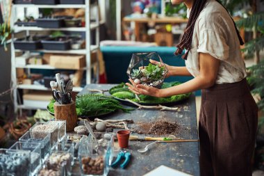 İki eliyle birden çok yüzlü floraryum tutan örgü örgülü bir kadın.