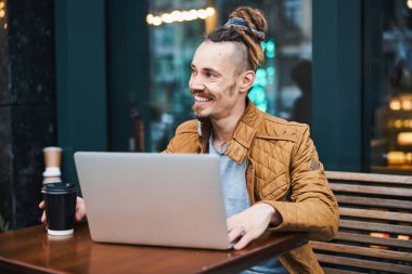 Dışarıda dizüstü bilgisayarda çalışan gülümseyen genç adam.