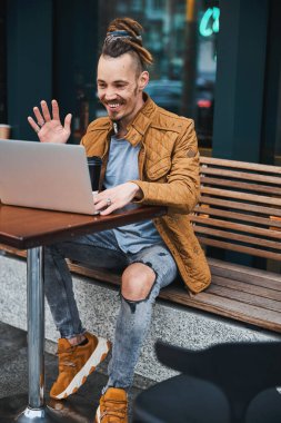 Neşeli hipster sokak kafesinde internetten iletişim kuruyor.
