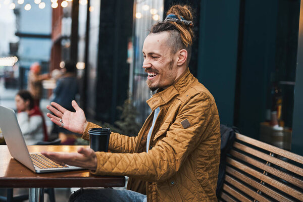 Cheerful young man using notebook in street cafe