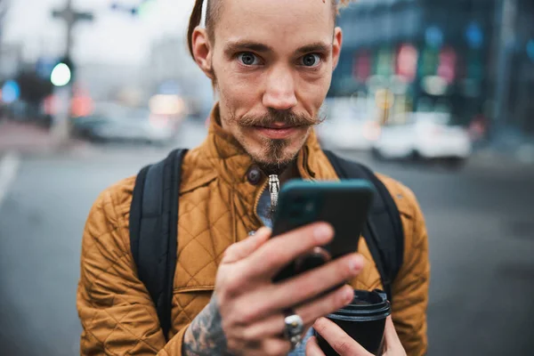 Veselý mladý vousatý muž pomocí mobilního telefonu venku — Stock fotografie