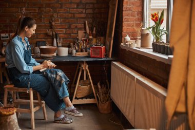 Genç beyaz kadın zanaatkar çömlek atölyesinde vakit geçiriyor.