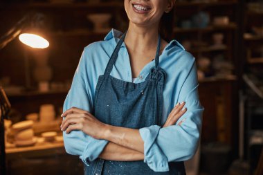 Çanak çömlek atölyesinde fotoğraf makinesine poz veren tanınmamış mutlu bir zanaatkar kadın.