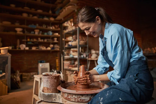 Смеющаяся кавказская ремесленница, моделирующая глиняную посуду в керамической мастерской — стоковое фото