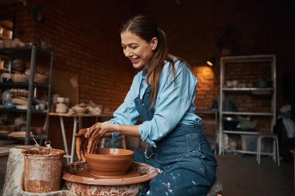 Молодой кавказский очаровательный керамик в фартуке моделирует глиняную чашу в керамической мастерской — стоковое фото