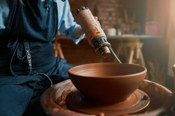 Unerkannte Kunsthandwerkerin mit Pusteblume in der Hand arbeitet in Töpferei mit frischem, feuchtem Tongeschirr — Stockfoto