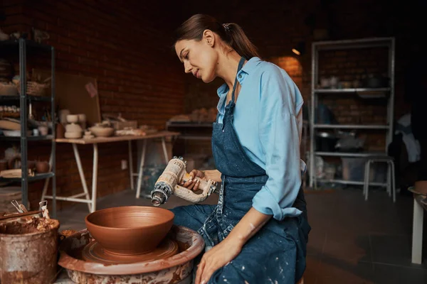 Brune femme artisan modélisant vaisselle en céramique sur équipement spécial en atelier de poterie — Photo