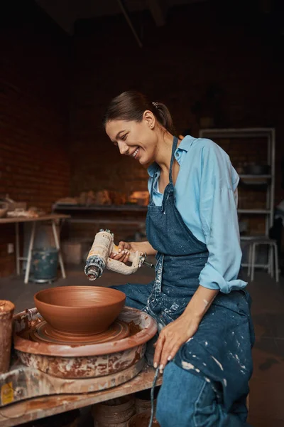 Fiatal vidám kézműves nő visel kötény dolgozik kerámia kerék friss nedves agyag a művészeti stúdióban — Stock Fotó