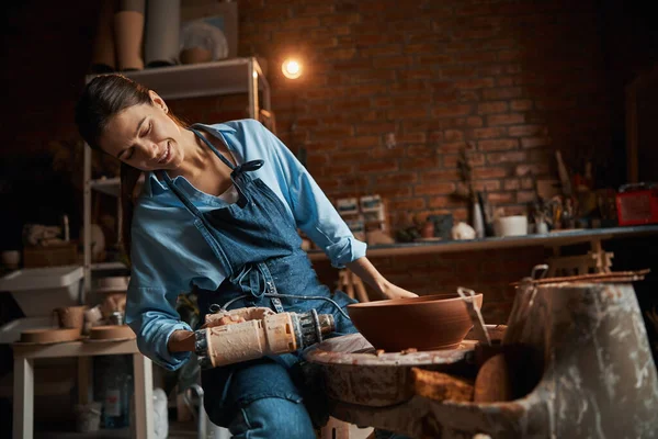 Vajilla de modelado artesanal femenina profesional en rueda de cerámica mientras usa una herramienta especial en el estudio de arte —  Fotos de Stock