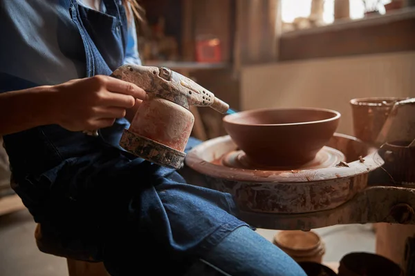 Элегантная ремесленница в фартуке делает глиняную чашу на гончарном круге в мастерской — стоковое фото