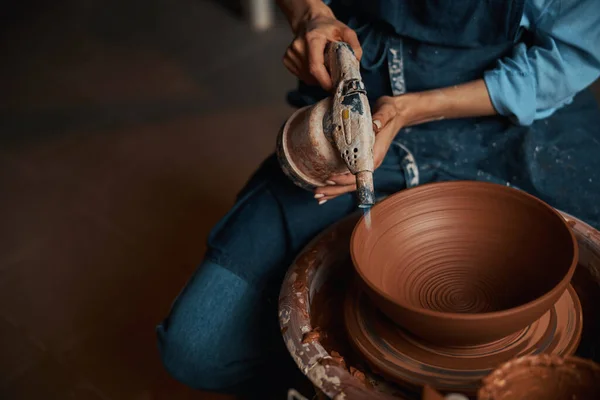 Nierozpoznana rzemieślniczka w fartuchu pracująca na kole ceramicznym podczas wykonywania zastaw stołowych w nowoczesnym warsztacie — Zdjęcie stockowe