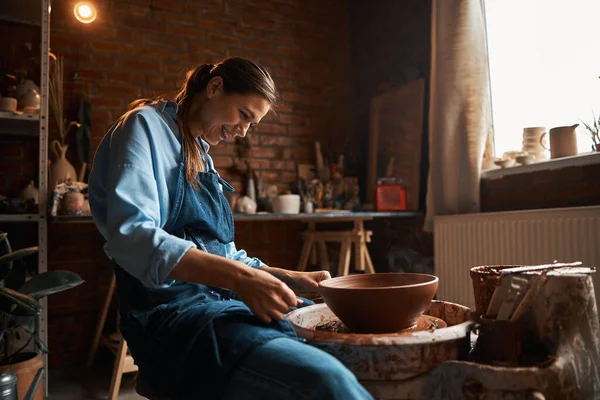 Felice sorridente donna artigianale caucasica durante il processo di produzione di stoviglie in argilla in laboratorio di ceramica — Foto Stock
