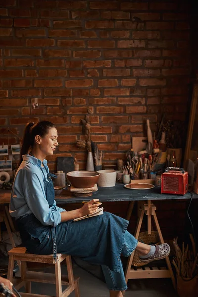 Szczęśliwa uśmiechnięta elegancka kobieta w fartuchu pracująca w pracowni artystycznej — Zdjęcie stockowe