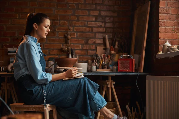 Felice positivo premuroso donna artigianale caucasica scrivere qualcosa in laboratorio di ceramica — Foto Stock