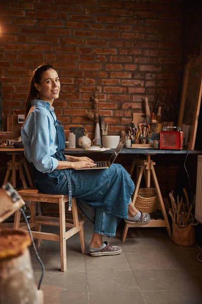 Hermosa mujer caucásica artesana con delantal mirando y posando en la cámara fotográfica en el estudio de arte — Foto de Stock
