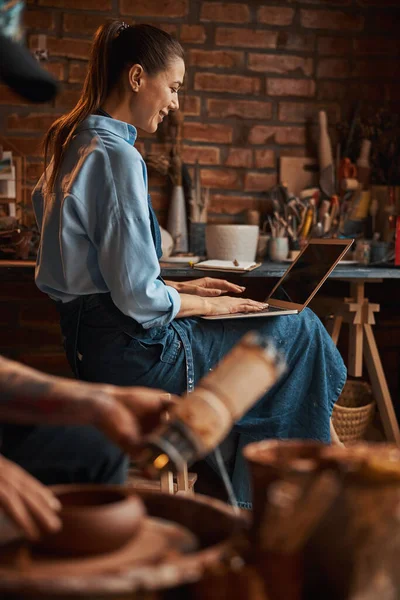 Hermosa mujer artesanal positiva usando delantal pasar tiempo en el taller de cerámica — Foto de Stock