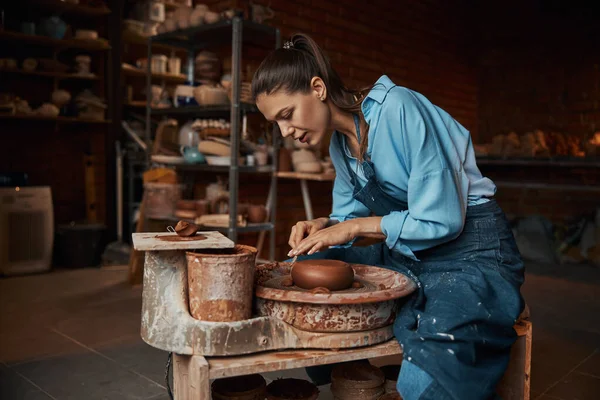 Красивая элегантная ремесленница, работающая со свежей влажной глиной на специальном оборудовании в керамической мастерской — стоковое фото