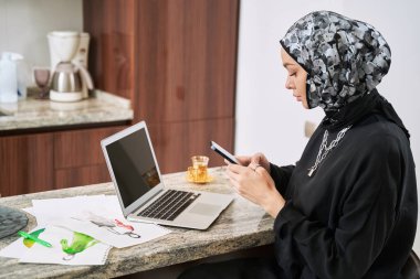 Cihazları olan genç Müslüman kadın evde geleneksel moda yaratıyor.