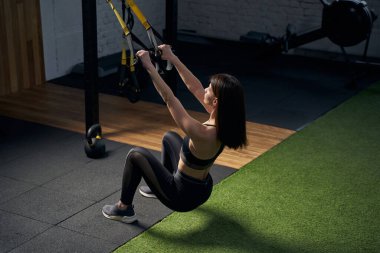 Spor salonunda asma antrenmanı kayışları kullanan atletik kadın.