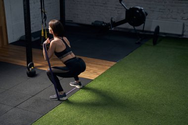 Sportif kadın spor salonunda fitness bandıyla çömeliyor.