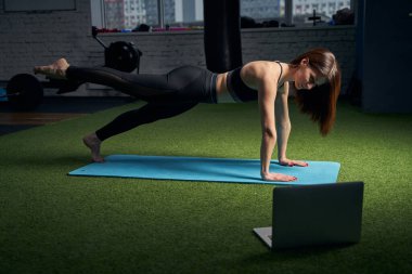 Kadın spor yapıyor ve spor salonunda dizüstü bilgisayar kullanıyor.