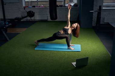 Yoga yapan ve bilgisayarlı spor salonu kullanan bir kadın.