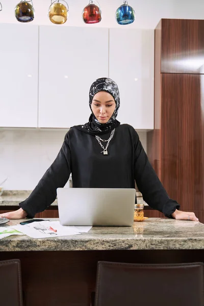 Uvolněná muslimka pomocí gadgets v kuchyni — Stock fotografie