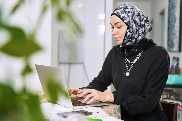 Žena muslim návrhářka pracující na notebooku v kuchyni — Stock fotografie