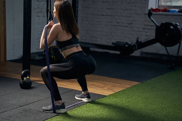 Sportliche Frau macht Kniebeugen mit Fitnessband im Fitnessstudio — Stockfoto