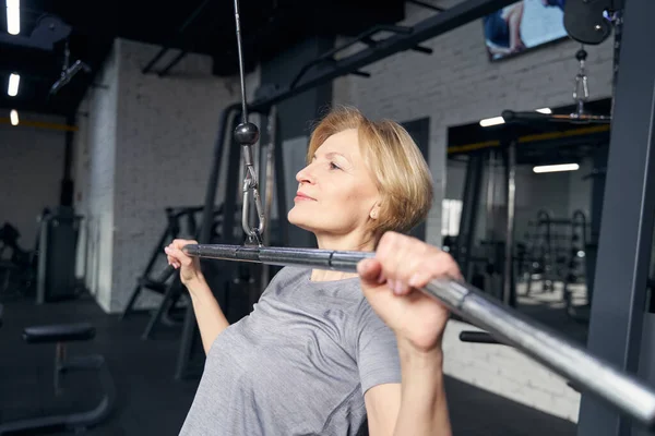 Mujer usando máquina de extracción de lat en el gimnasio — Foto de Stock