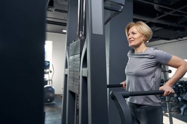 Spor kıyafetli neşeli bir kadın spor salonunda egzersiz yapıyor.