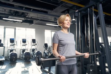 Spor salonunda halterle egzersiz yapan neşeli bir kadın.